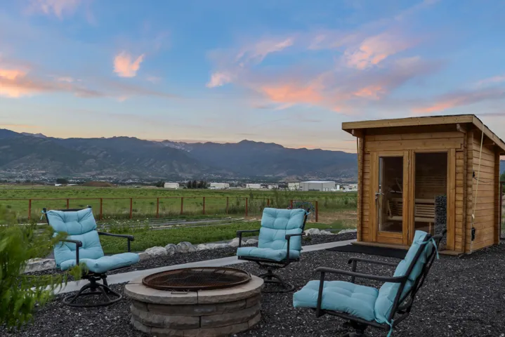 Outdoor living area featuring a stone-clad fire pit, a gravel patio, and a standalone wooden sauna structure with glass-paned doors