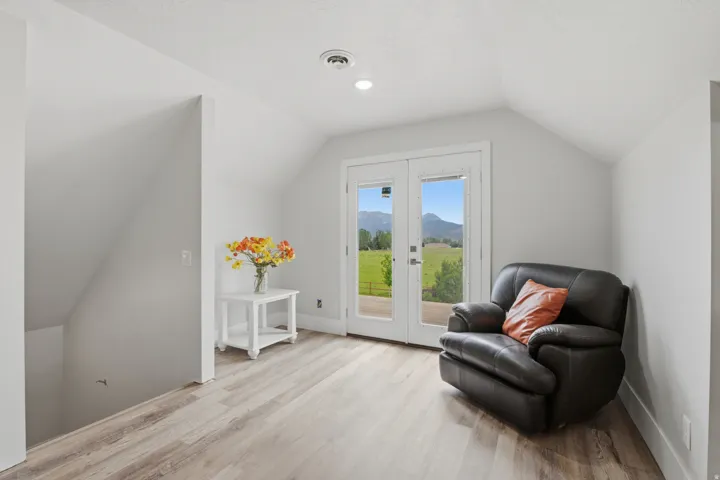 Upper-level space featuring vaulted ceilings, wood-finish flooring, recessed lighting, and white French doors opening to an exterior landscape