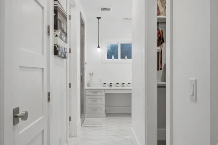 White bathroom vanity with built-in desk, under-mount sink, and contemporary pendant lighting