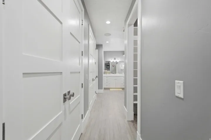 Hallway featuring light wood-finish flooring, white paneled doors with brushed nickel hardware, light grey painted walls, and recessed lighting
