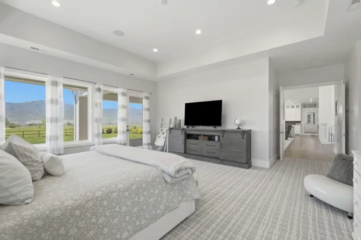 Spacious bedroom featuring a series of large windows, recessed ceiling lighting, tray ceiling, and light-toned patterned carpeting