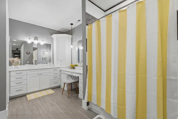 Bathroom featuring white cabinetry, wood-finish flooring, dual vanity sinks, and a built-in makeup desk