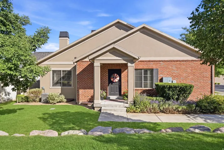 Brick and stucco exterior featuring a covered entry, mature landscaping, a manicured lawn, and a sidewalk leading to the front door