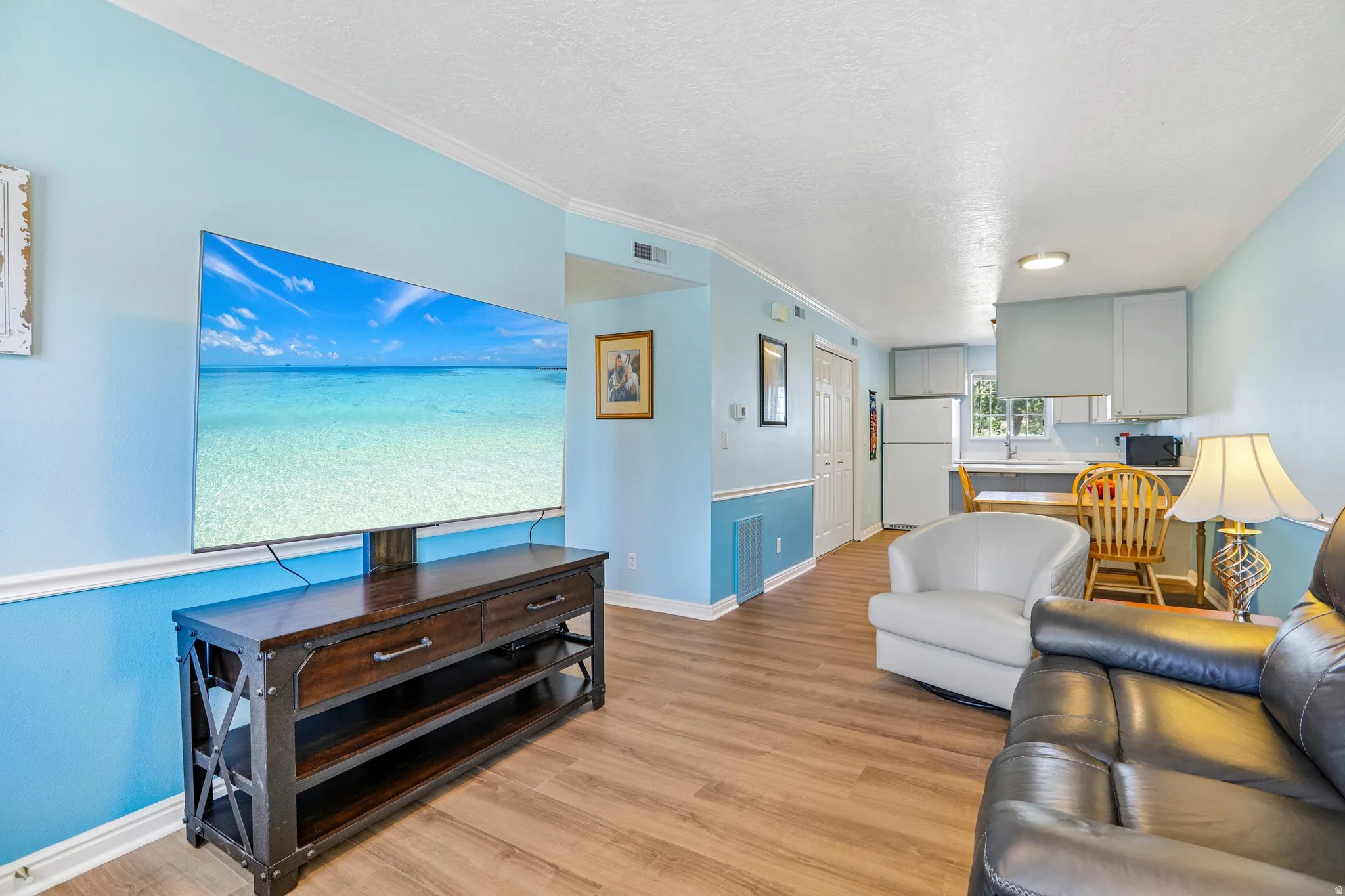Open-concept living area featuring wood-finish flooring, light blue wall paint with white trim, and a kitchen area with white cabinetry and a built-in countertop