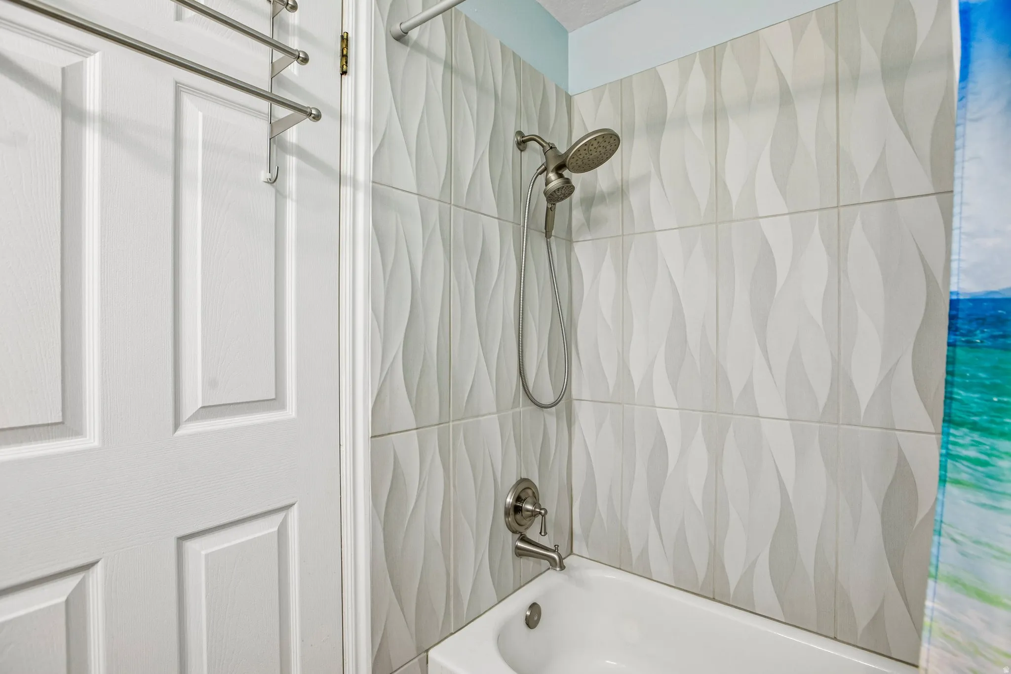 Shower with textured white tile surround, brushed nickel fixtures, and a classic white bathtub