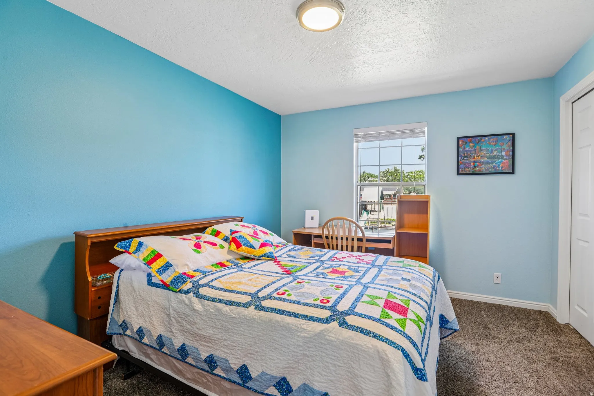 Bedroom with light blue walls, a window providing natural light, and plush grey carpeting