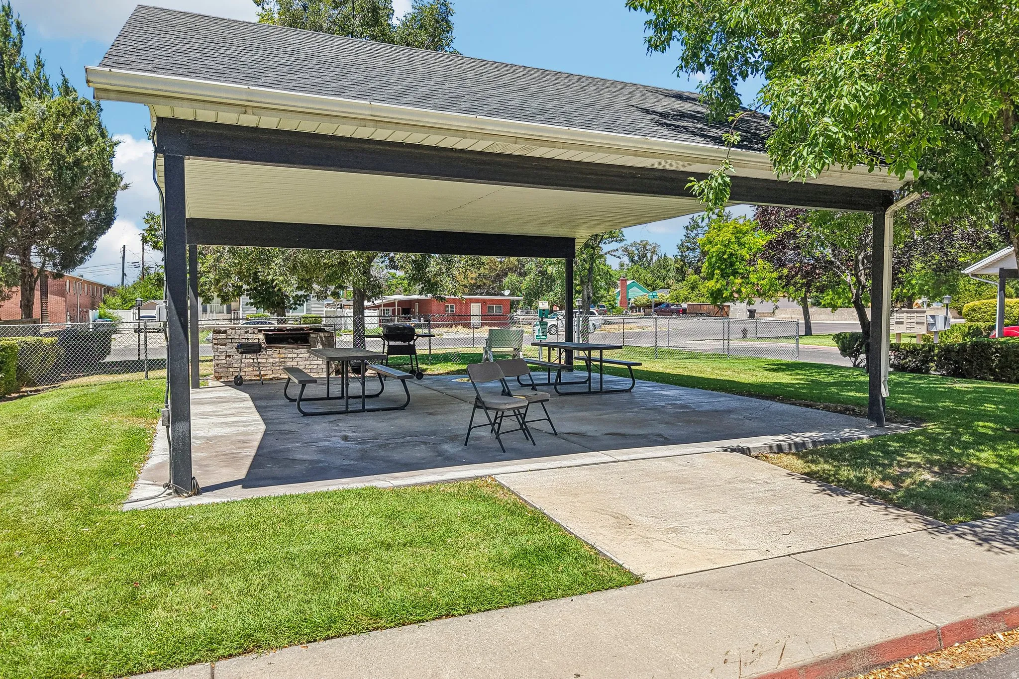 Covered outdoor patio with a concrete slab, integrated brick barbecue, and surrounding manicured lawn