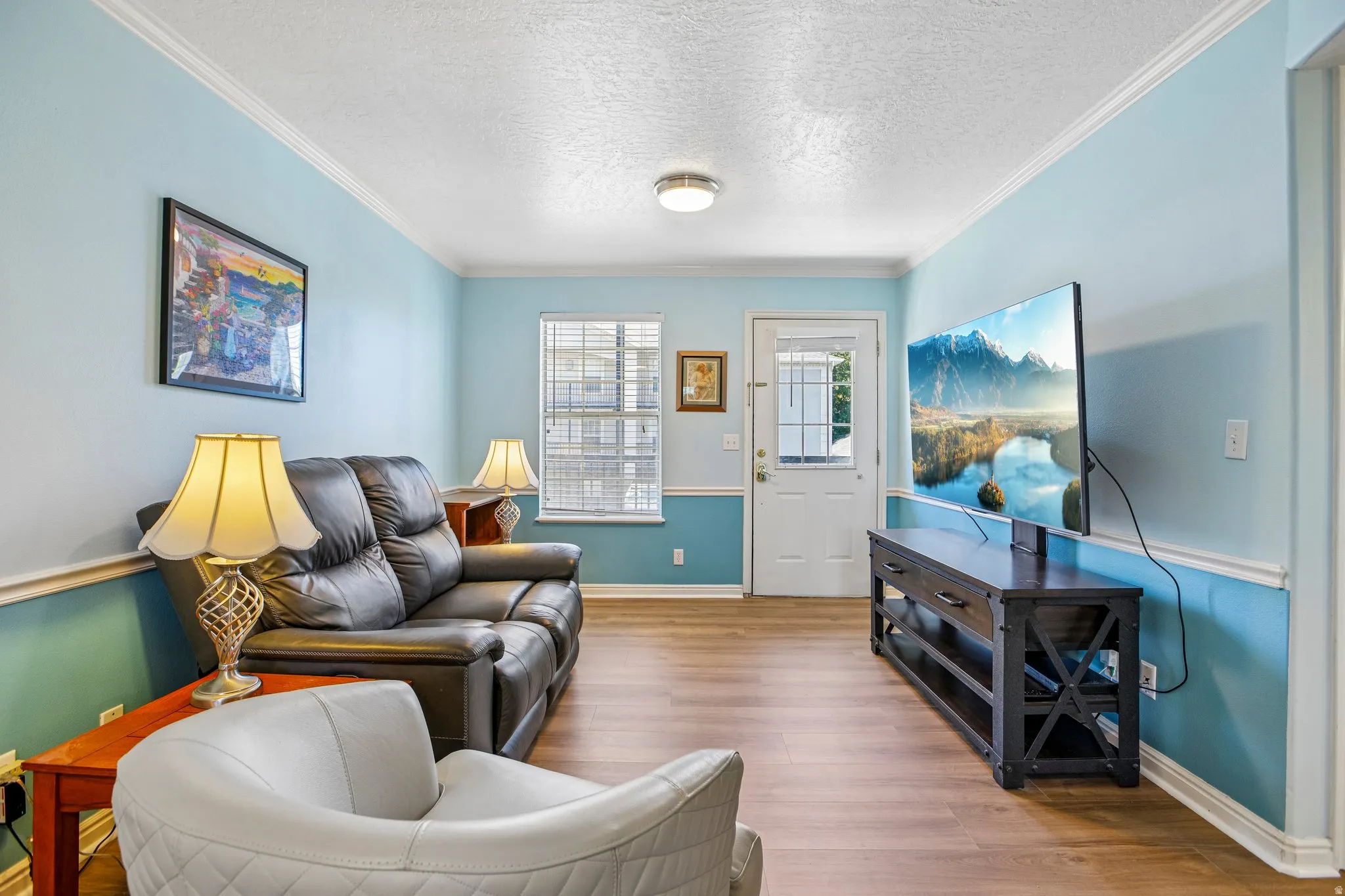 Living area featuring wood-finish flooring, light blue wall paint, white crown molding, and a white entry door with frosted glass panes