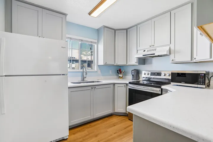 Kitchen featuring light gray cabinetry, white countertops, stainless steel appliances, wood-finish flooring, and a window above the sink