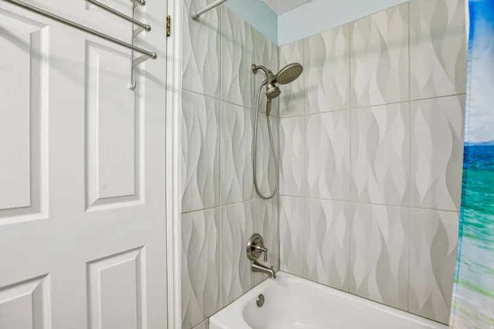 Shower with textured white tile surround, brushed nickel fixtures, and a classic white bathtub