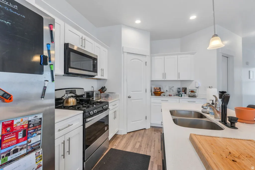 Contemporary kitchen featuring white shaker cabinetry, stainless steel appliances, a double basin sink, light-toned countertops, and wood-finish flooring