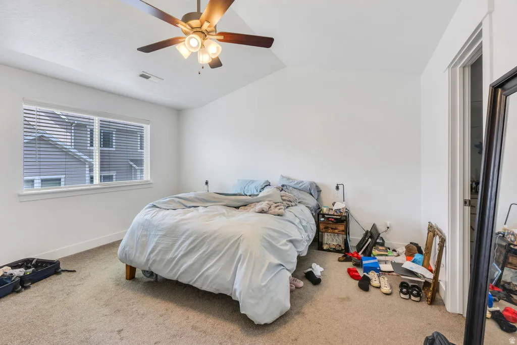 Carpeted bedroom featuring a vaulted ceiling with a ceiling fan light fixture, a window with horizontal blinds, and a white interior door frame
