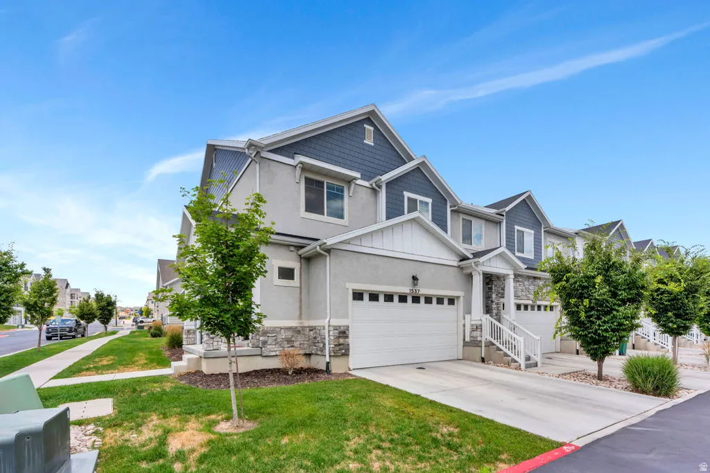 Contemporary townhome featuring a stucco and stone facade, a two-car garage, and a covered entryway