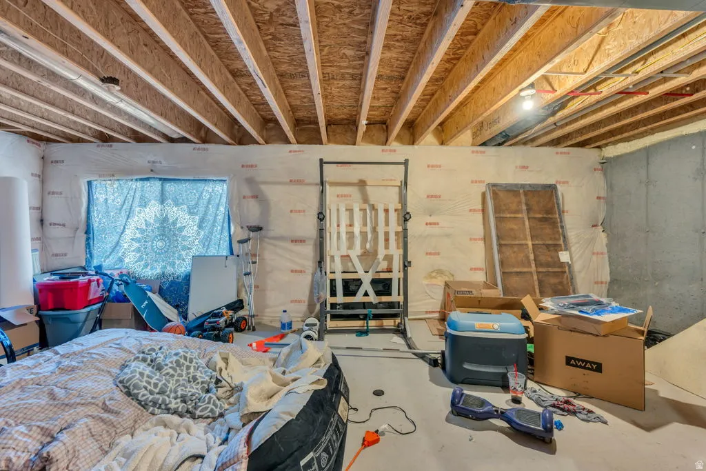 Unfinished basement space featuring exposed wood joists, a concrete foundation wall, and a window opening