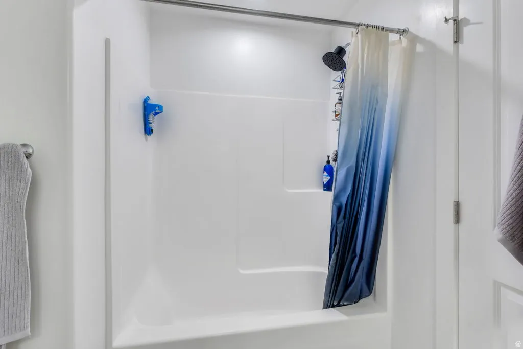 White fiberglass shower/tub combination with a dark-finish shower head and a curved shower rod