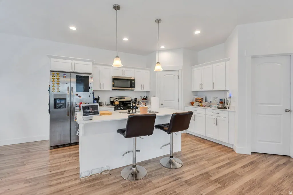 Open-concept kitchen featuring an island with pendant lighting, white cabinetry, stainless steel appliances, and wood-finish flooring