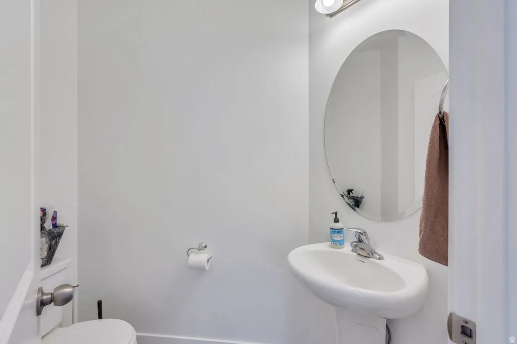 Pedestal sink with chrome faucet, oval wall mirror, and modern overhead lighting