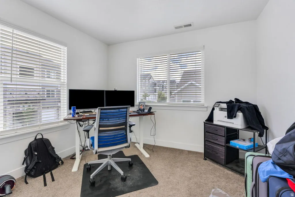 Bright room featuring two large windows with blinds, carpet flooring, white walls, and a visible ceiling vent