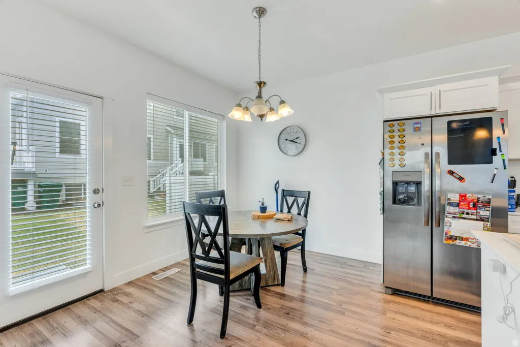 Bright dining area with wood-finish flooring, featuring a glass-paned exterior door, a large window, a ceiling-mounted light fixture, and white cabinetry