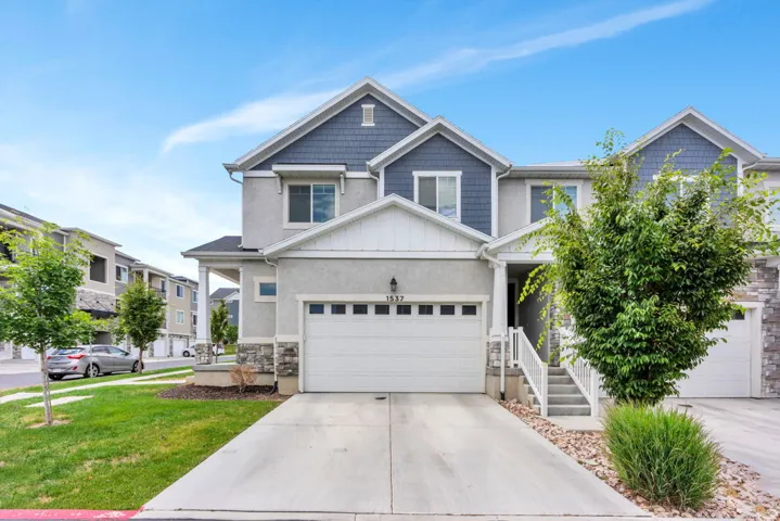 Two-story townhouse exterior with a light gray stucco finish and blue shingle accents