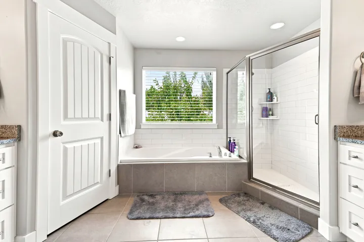 Bathroom featuring a built-in soaking tub with tile surround, a glass-enclosed shower with subway tile, a window with blinds, and recessed lighting