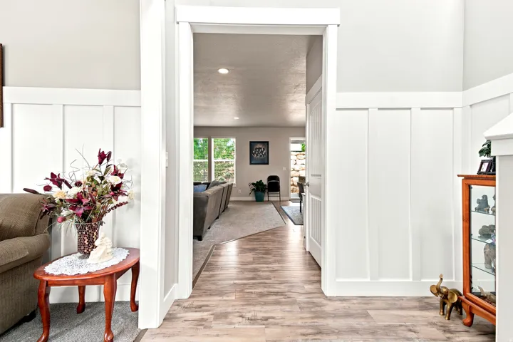 Entryway featuring wood-finish flooring, white wainscoting, and an open doorway leading to a carpeted living area with abundant natural light