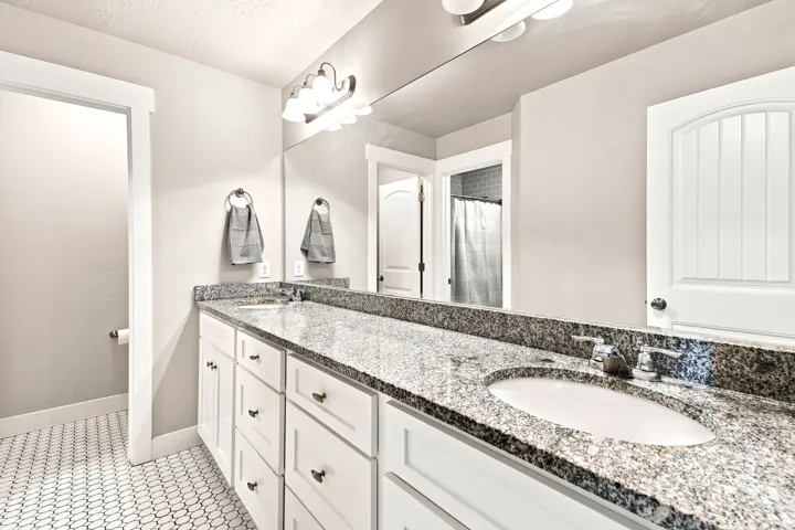 Spacious bathroom vanity featuring a dual sink design, granite countertop, and white cabinetry with dark hardware