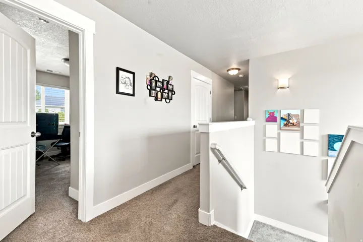 Upper-level hallway featuring neutral wall paint, carpet flooring, a white paneled door, and a staircase with a white railing