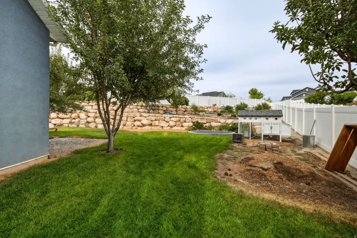 Expansive backyard featuring a lush lawn area, mature trees, and a terraced rock retaining wall