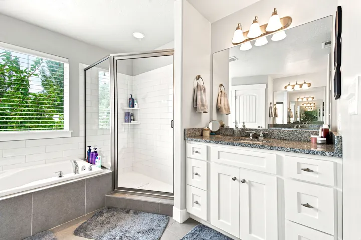 Spacious bathroom featuring a dual vanity with a granite countertop, a large mirror, a separate soaking tub with tiled surround, and a walk-in shower with subway tile