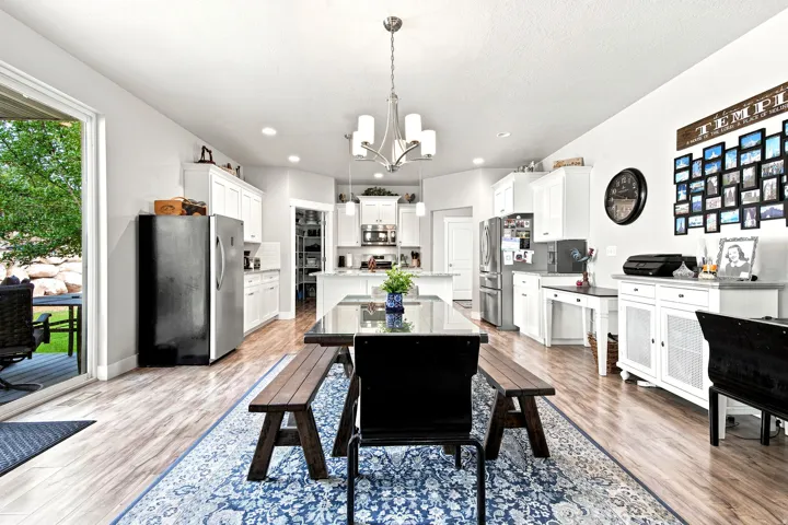 Spacious dining area featuring wood-finish flooring, a modern chandelier, and a sliding glass door providing access to an outdoor patio