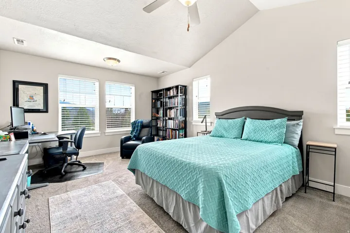 Carpeted room featuring a vaulted ceiling with a flush-mount light fixture and ceiling fan, multiple windows with blinds, a built-in bookshelf, and a built-in desk area