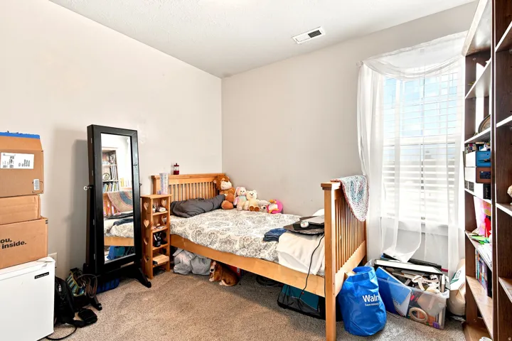 Carpeted bedroom featuring a large window with blinds, a ceiling air vent, and light-toned walls