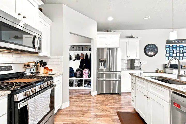 Modern kitchen featuring stainless steel appliances, white cabinetry, granite countertops, and wood-finish flooring