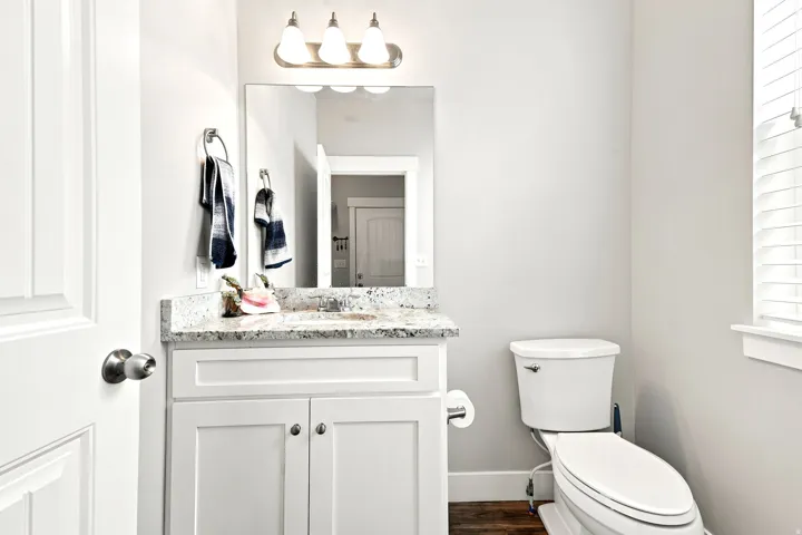 Bathroom featuring white shaker-style vanity with a stone-finish countertop, single basin sink, and an overhead three-light fixture