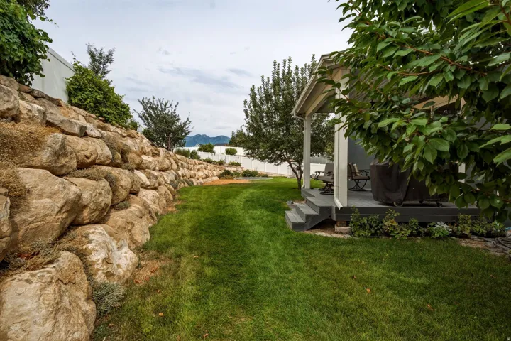 Expansive terraced yard featuring a natural stone retaining wall, verdant lawn, covered porch with columns, and mature trees