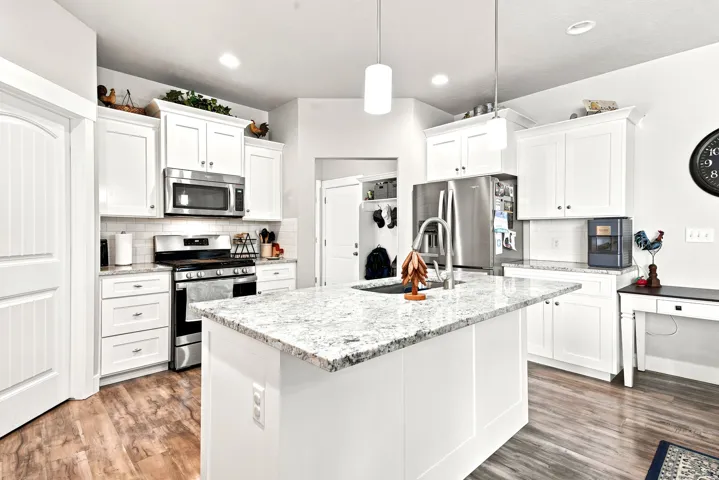Kitchen featuring a spacious island with a light-toned granite countertop, white cabinetry, stainless steel appliances, wood-finish flooring, and recessed lighting