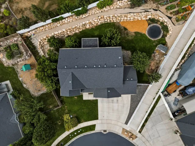 Expansive property featuring a dark shingle roof, concrete driveway, and mature landscaping