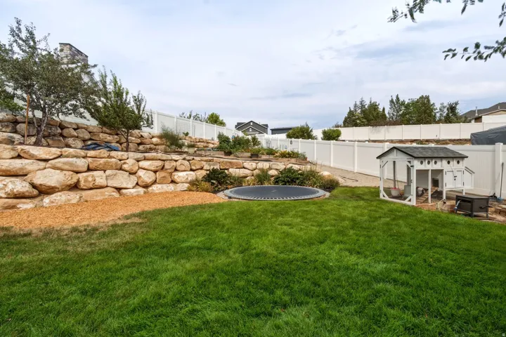 Expansive backyard featuring a lush green lawn, tiered rock retaining walls, and mature landscaping