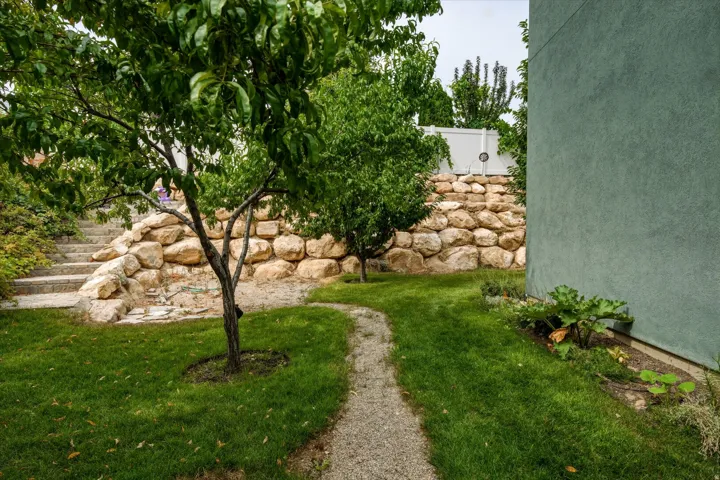 Landscaped garden featuring a gravel pathway, mature trees, a stone retaining wall, and concrete steps