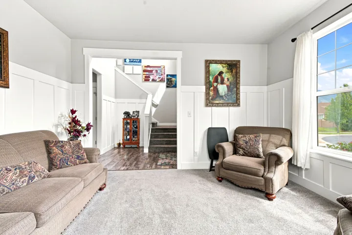 Bright living space featuring a window with exterior views, board and batten wall detailing, light gray painted walls, and soft carpet flooring