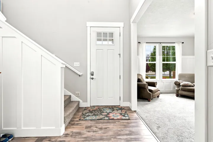 Entryway featuring a paneled front door with upper glass inserts, wood-finish flooring, a carpeted staircase with white wainscoting, and a handrail