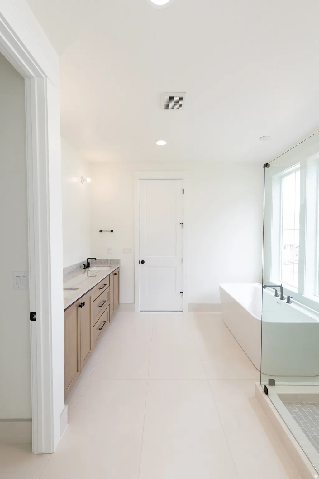 Dual vanity with stone countertop, freestanding soaking tub, glass-enclosed shower, and recessed lighting