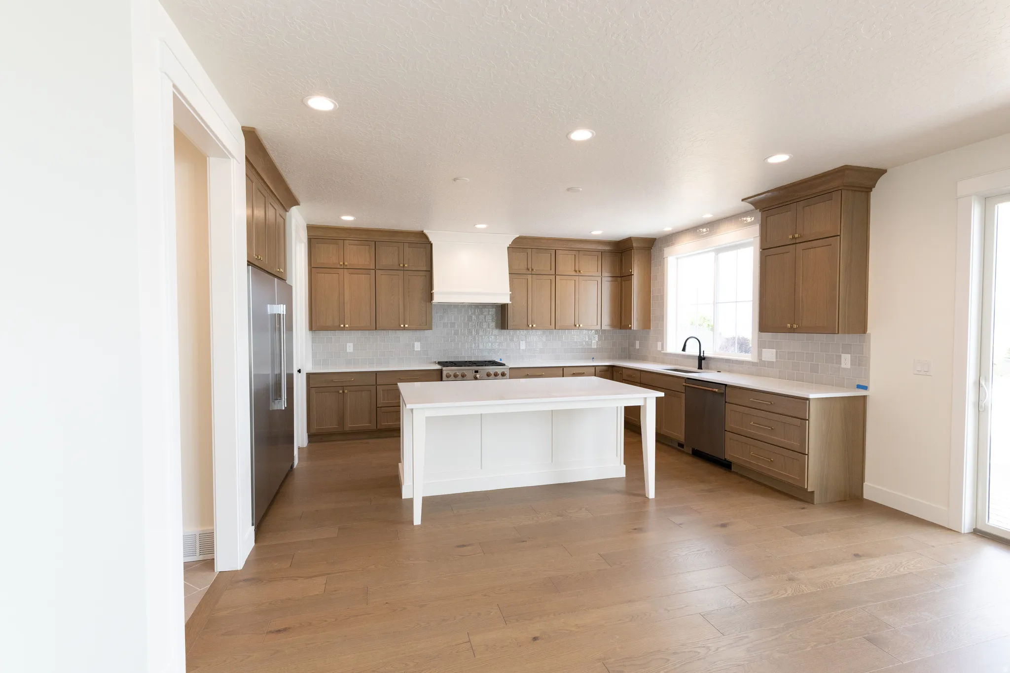 Kitchen featuring wood-finish flooring, white island, light wood cabinetry, recessed lighting, and stainless steel appliances