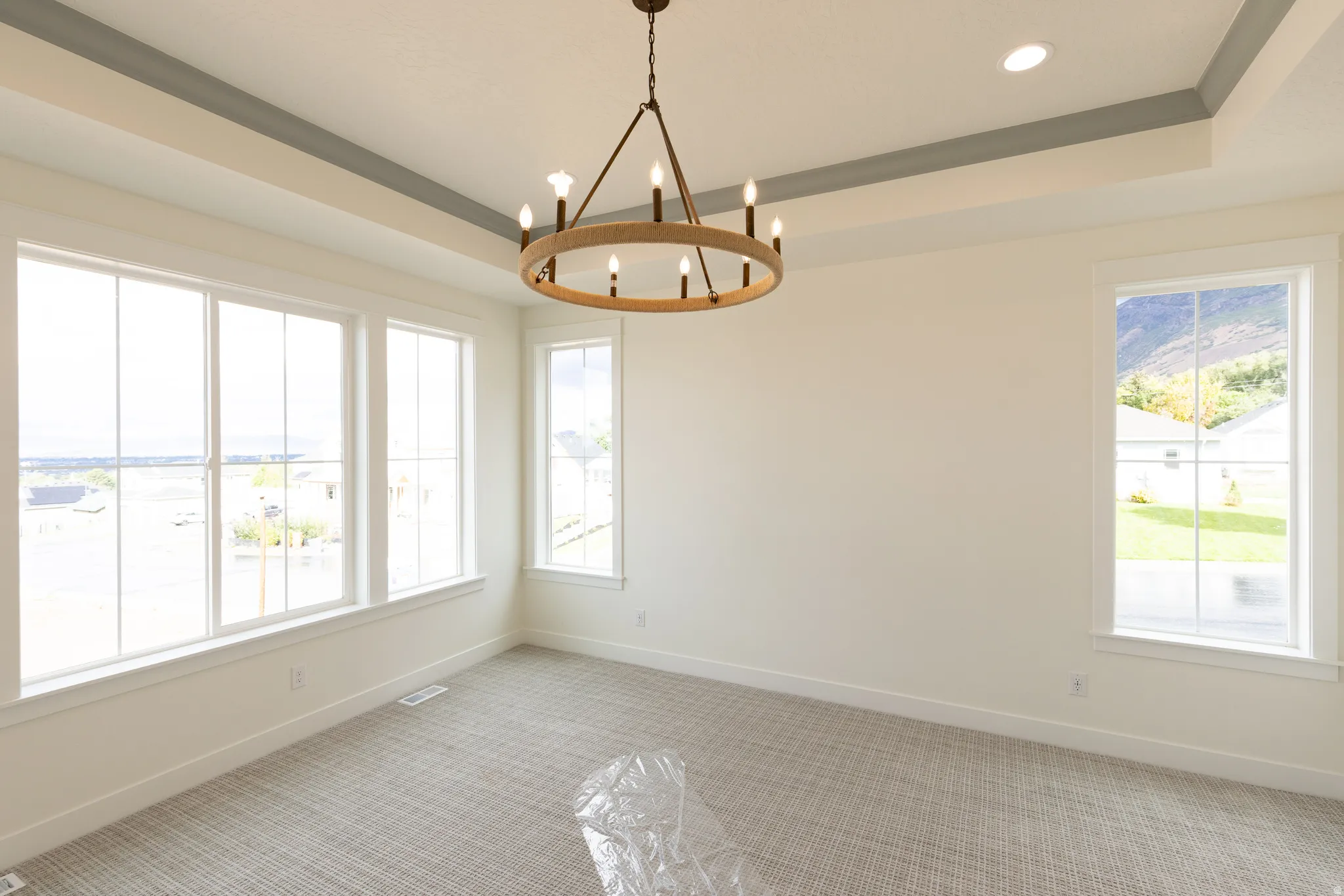 Tray ceiling with recessed lighting, large picture windows, wood-finish chandelier, and textured carpeting