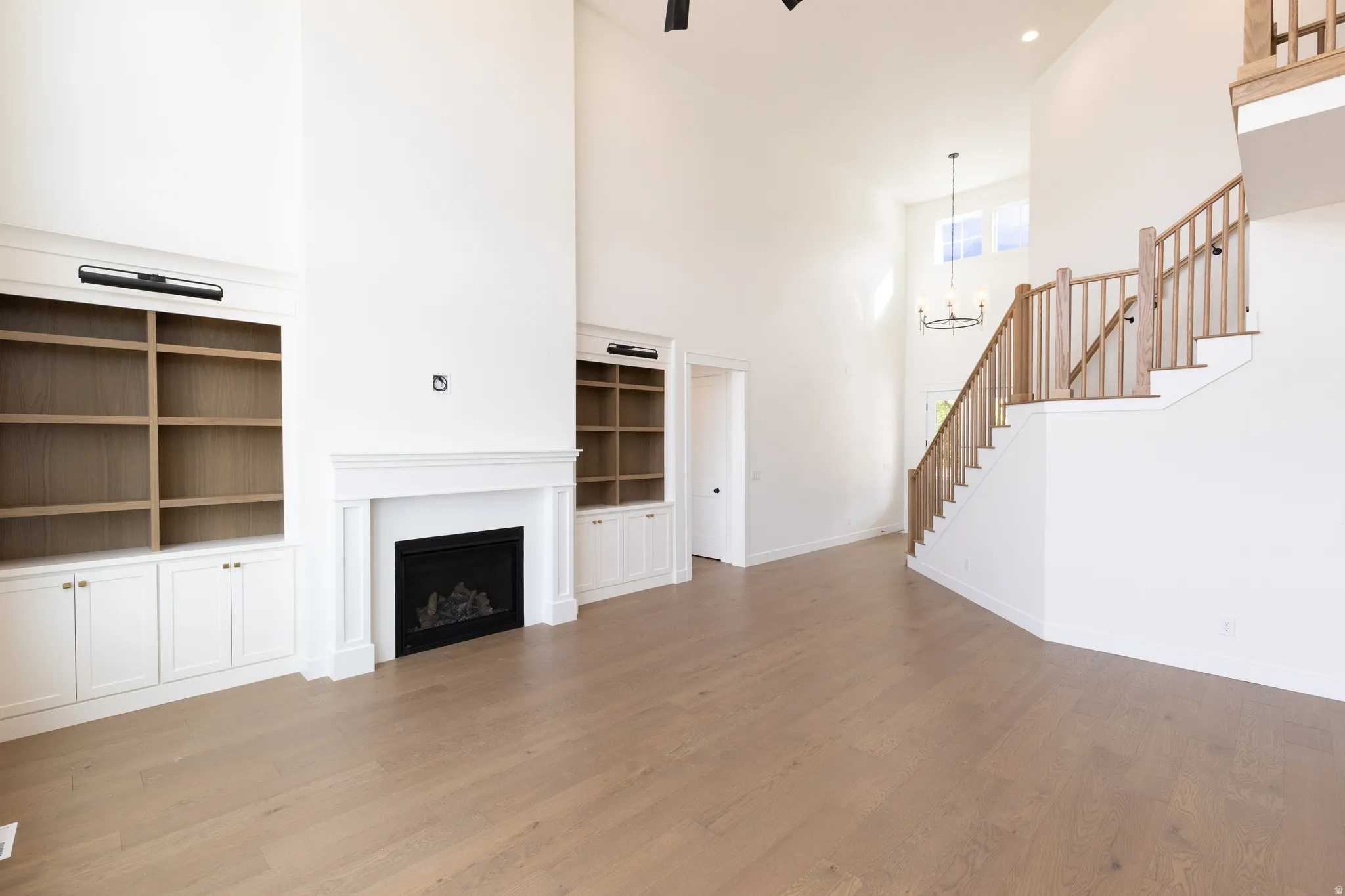 Spacious room featuring high ceilings, a fireplace with a classic mantel, built-in shelving, wood-finish flooring, and a staircase with wood railings