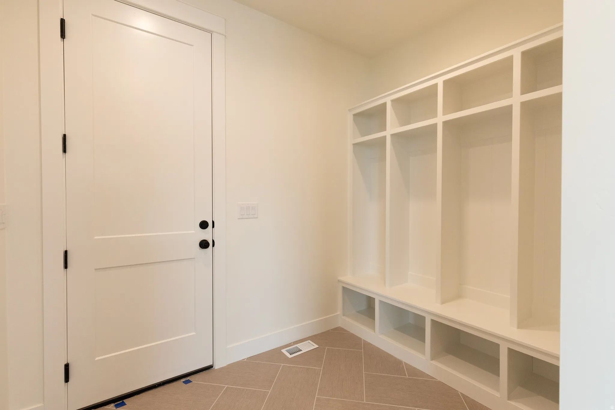 Entryway with built-in storage cubbies, bench seating, panel door, and herringbone tile flooring