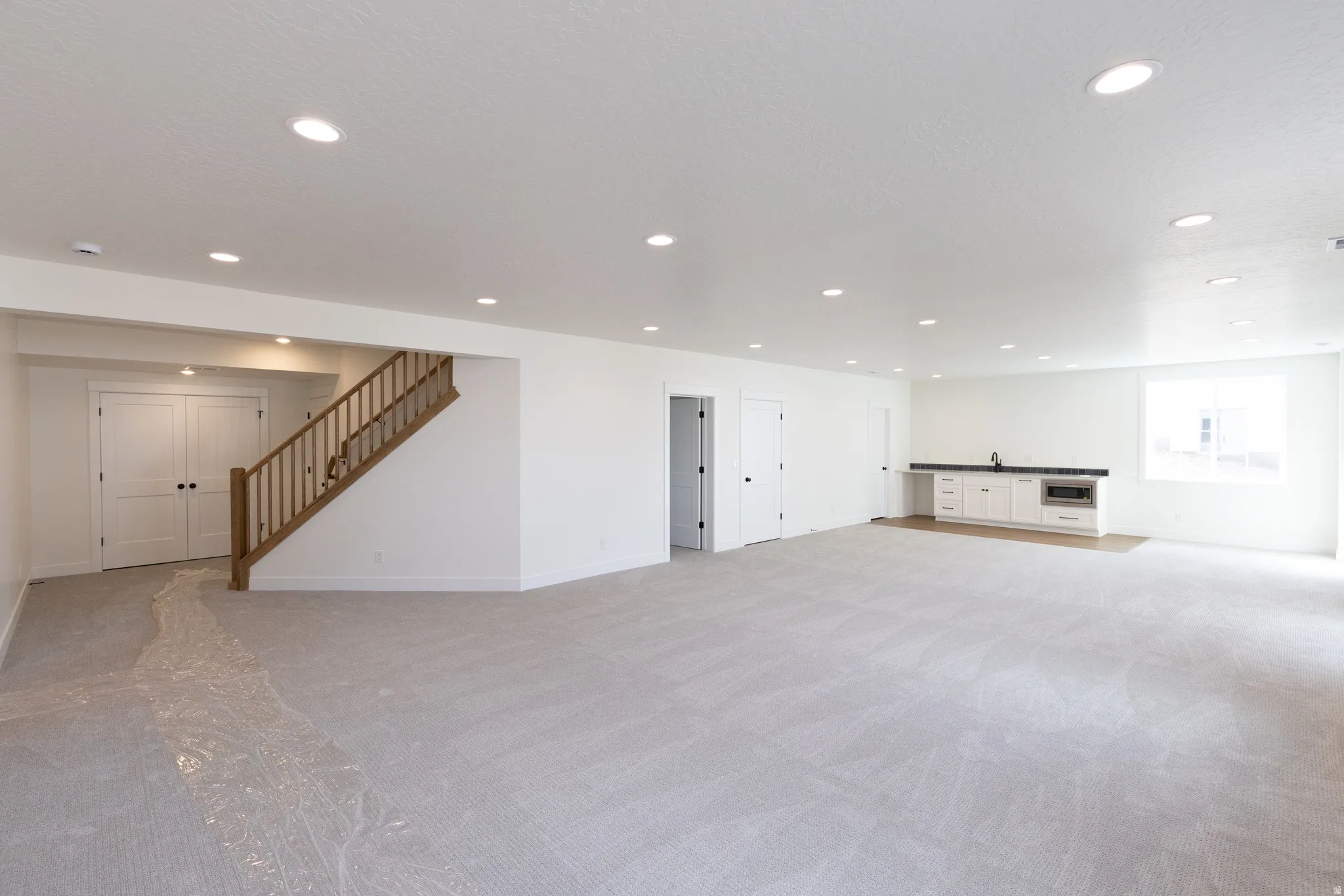 Spacious finished room featuring recessed lighting, a built-in wet bar with a sink and white cabinetry, and carpeted flooring