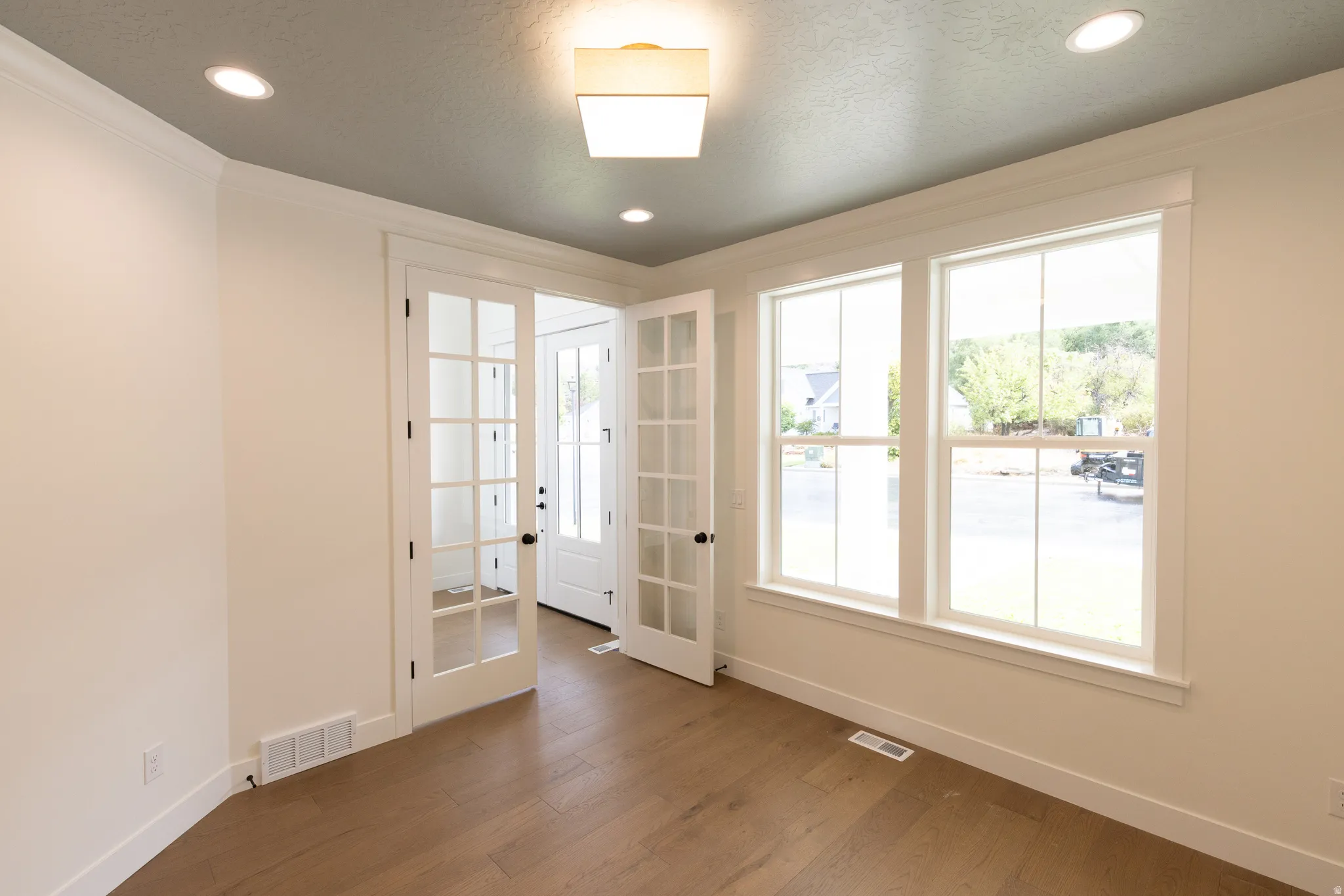 White French doors, recessed lighting, wood-finish flooring, two large windows, and crown molding
