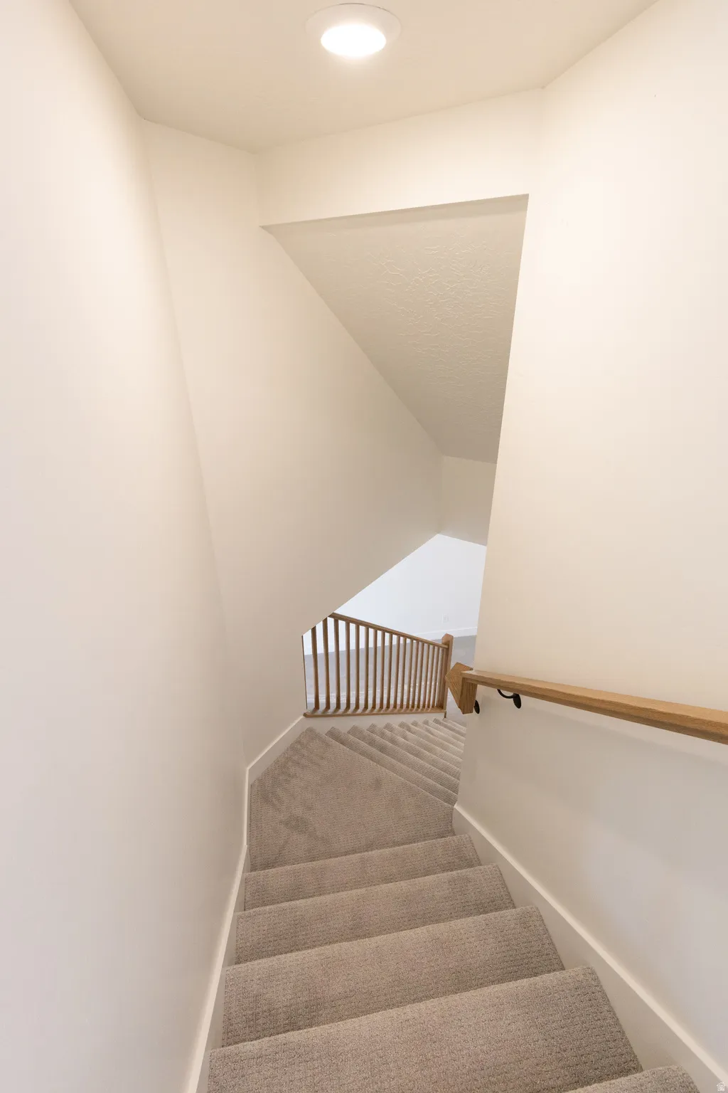 Carpeted staircase with light wood-tone handrail and vertical balusters